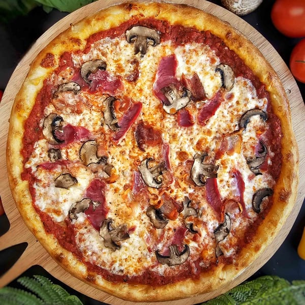 A freshly baked Bread Street Boys pizza with mushrooms and ham on a wooden board.