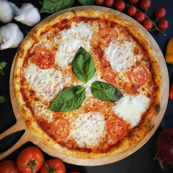 A Bread Street Boys Pizza with cheese, sliced tomatoes, and basil on a wooden peel.
