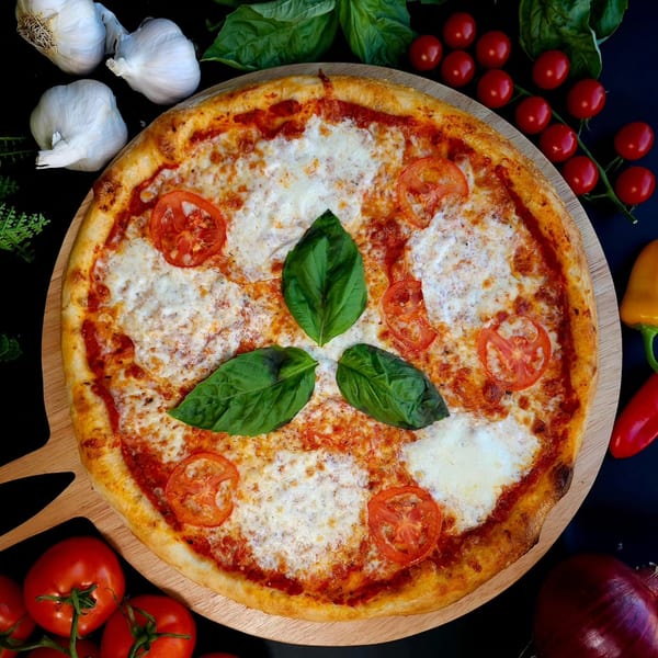 Overhead view of a Bread Street Boys pizza with tomatoes, basil, and garlic on a wooden board.