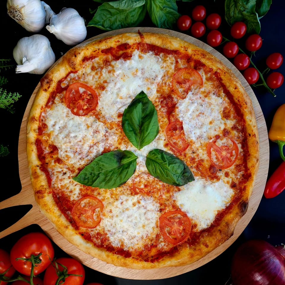 Overhead view of a Bread Street Boys pizza with tomatoes, basil, and garlic on a wooden board.
