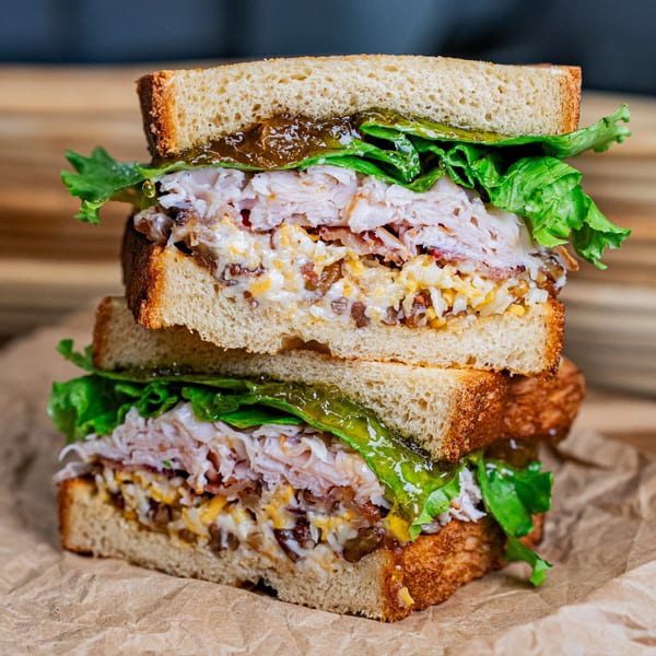 Two halves of a stacked turkey sandwich with lettuce, cheese, and relish on toasted bread.