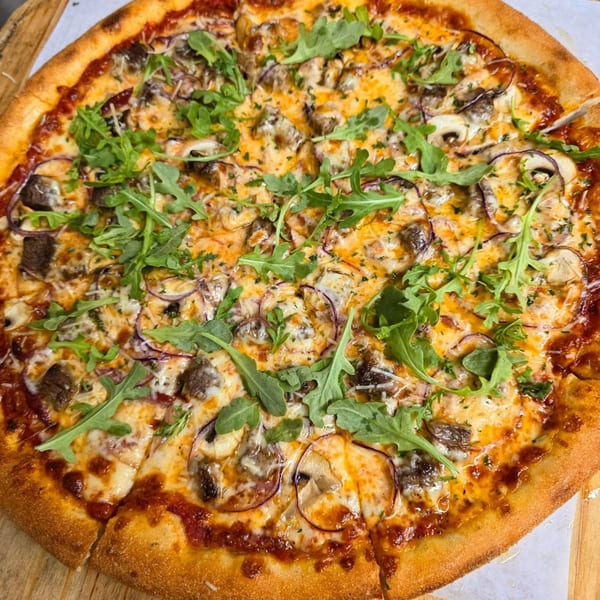 A freshly baked pizza from Bread Street Boys, topped with cheese, mushrooms, red onions, and arugula.