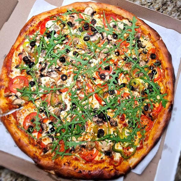 A large, freshly baked pizza from Bread Street Boys, topped with arugula, olives, mushrooms, and tomatoes.