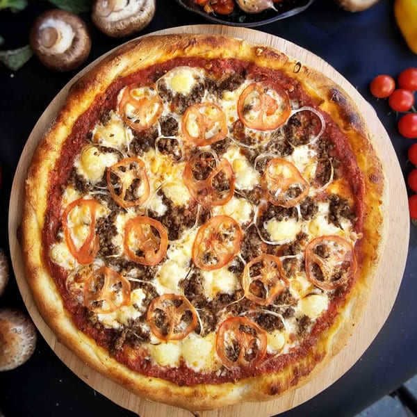 Overhead view of a Bread Street Boys pizza with ground meat, cheese, and tomato slices.